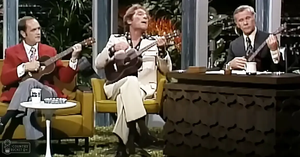 Musical performance in an indoor studio with greenery and a fire pit, evening lighting, and yellow armchairs.
