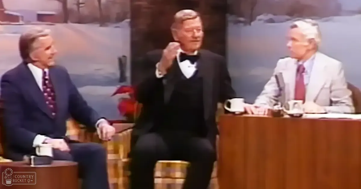 Three older adult males dressed in formal suits and ties, seated at a wooden table with mugs on it against a backdrop of snowy landscape.