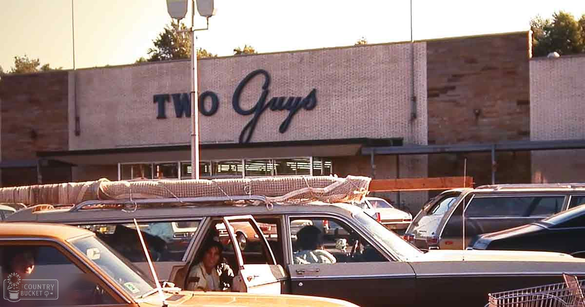 A parking lot scene outside 'Two Guys,' a grocery store, with various vehicles and an adult male child wearing a striped shirt standing near a car. The setting is mid-20th-century commercial architecture under warm morning or late afternoon light.