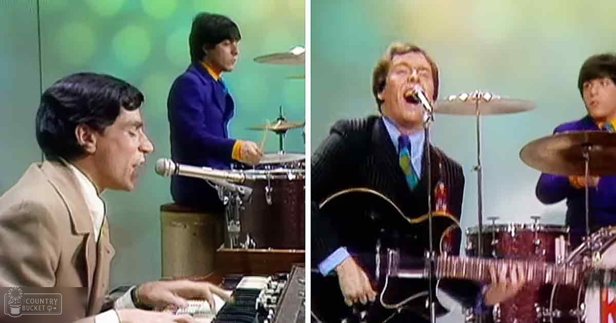 A musical performance with three young adult male musicians and a drummer in an indoor studio setting with plain green background, light-colored shirts, dark blue and purple suits, and a drum set.