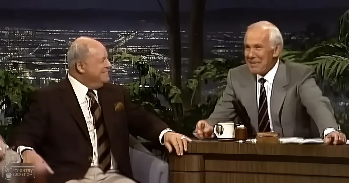 Two older adult males seated indoors during a talk show discussion; cityscape background suggests urban studio setting at night.