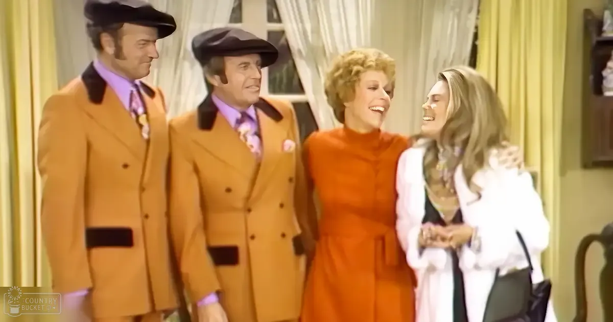 Four individuals dressed in formal attire are positioned together in an indoor setting with yellow curtains and wooden furniture.