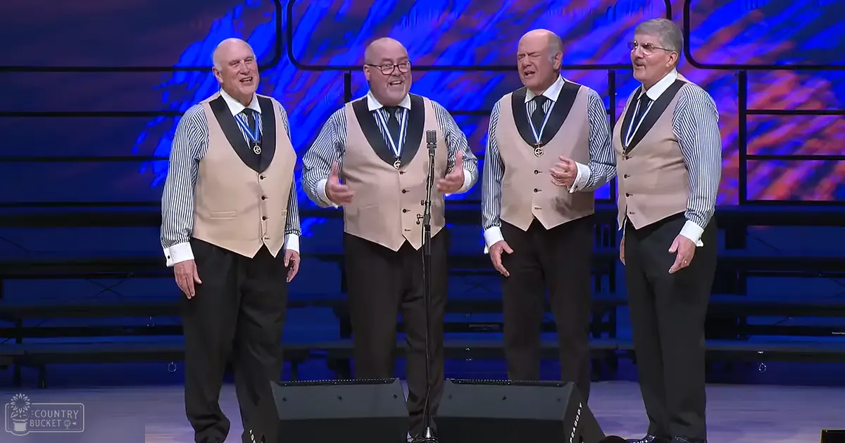A barbershop quartet performing on stage with stage lighting in an indoor venue.