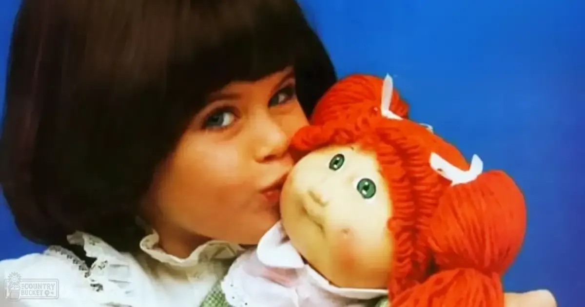 A child wearing a white lace-trimmed blouse holding a red-haired doll in an indoor setting with a plain blue backdrop.