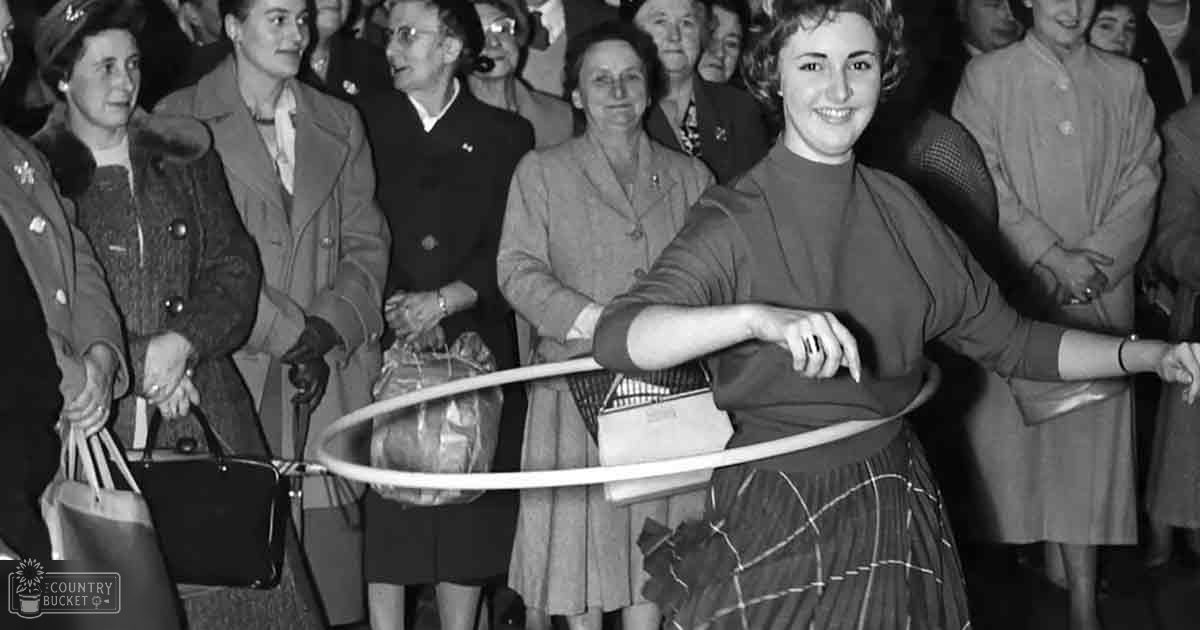 A young adult woman performs with a hula hoop at a public event, surrounded by spectators dressed in mid-20th-century attire.