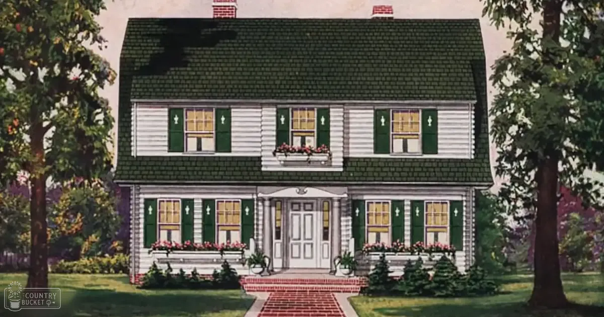 A two-story suburban house with white siding, dark green roof shingles, and a red brick pathway adorned with pink flowers, surrounded by well-maintained greenery in spring or summer.