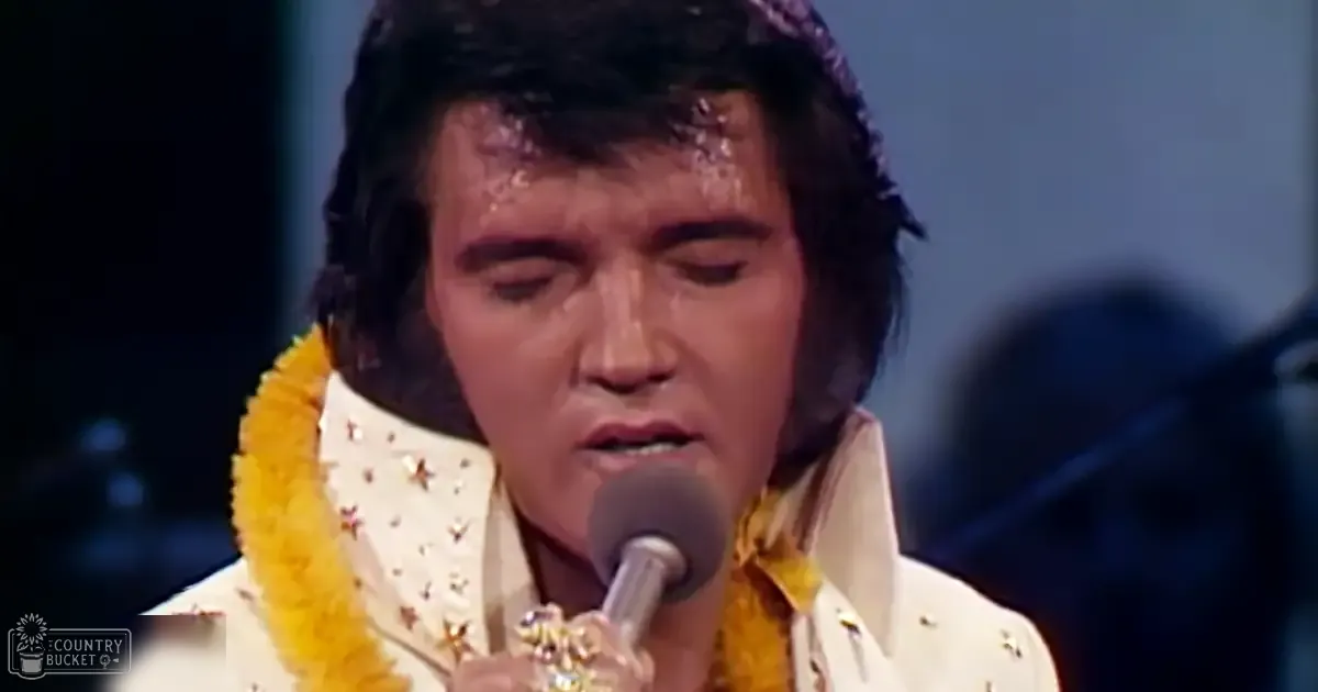 An adult male singer wearing a white mid-20th-century stage costume with gold star patterns and yellow accents, holding a microphone on an indoor performance stage.
