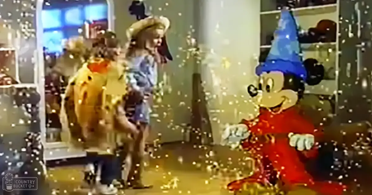 A child wearing a denim skirt and patterned top stands beside an adult in a wizard's robe inside a Disney-themed shopping mall display.