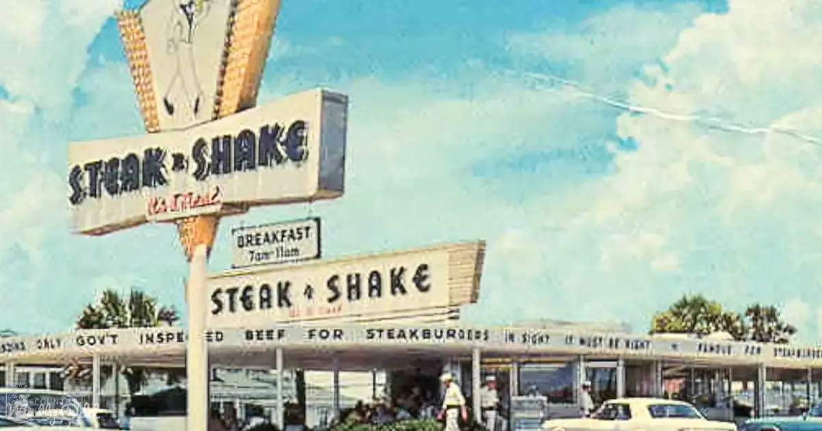 A Steak 'n Shake restaurant with a vintage car parked outside on an outdoor day with clear skies and trees in the background.
