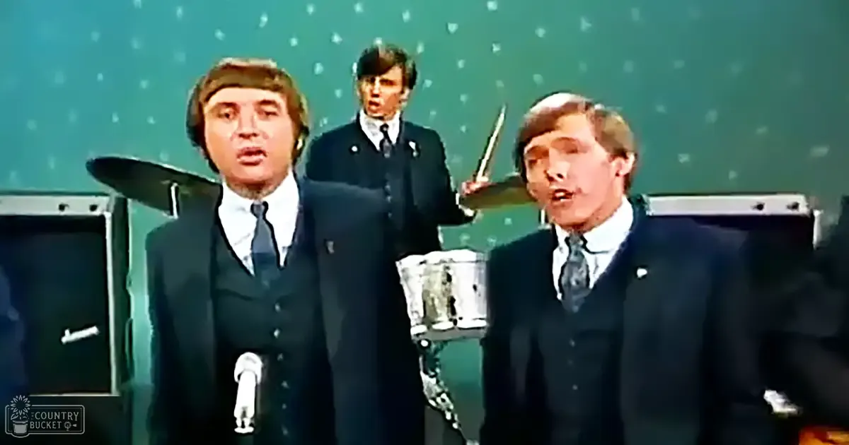 A musical performance scene with adult males in dark suits against a green backdrop, suggesting an indoor venue.