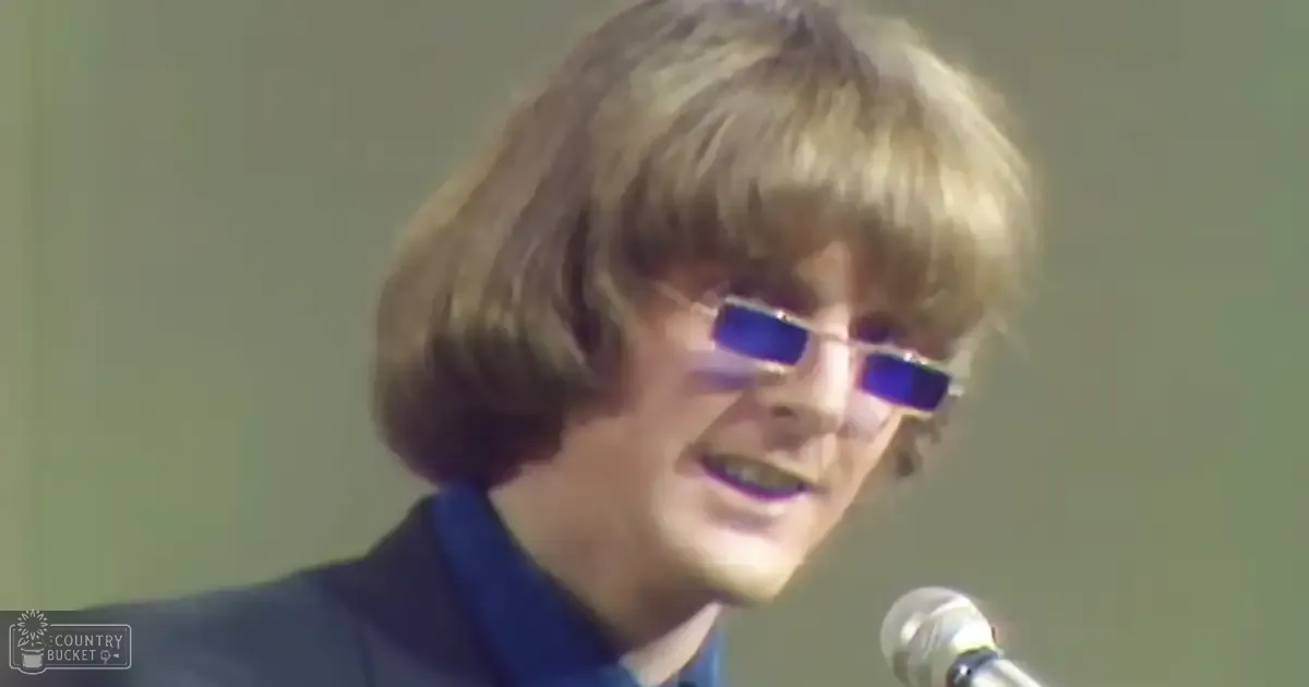 A young adult male singer in a dark suit jacket, performing at an event or concert with a microphone and text reading 'Madly Odd' on the bottom left corner.