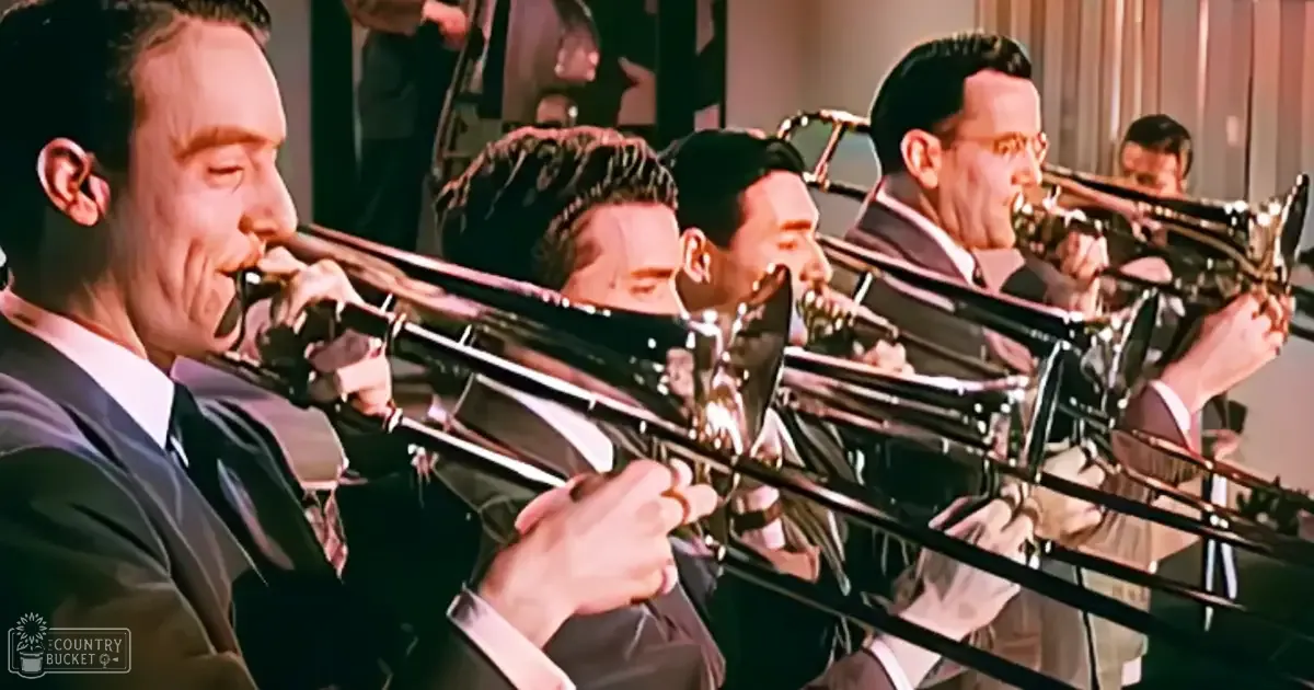 A group of young adult male musicians in dark suits playing trombones indoors, possibly in a concert hall or performance venue.