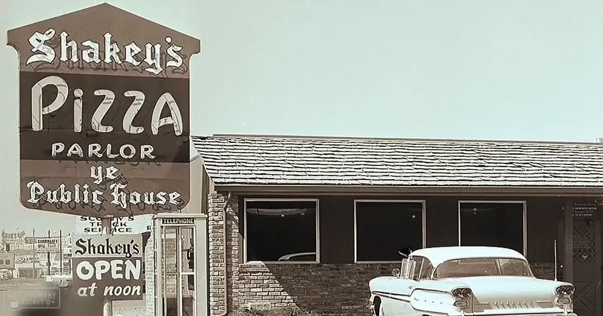Shakey's Pizza Parlor sign indicating it is open at noon in a suburban outdoor setting with muted tones typical of vintage photographs.
