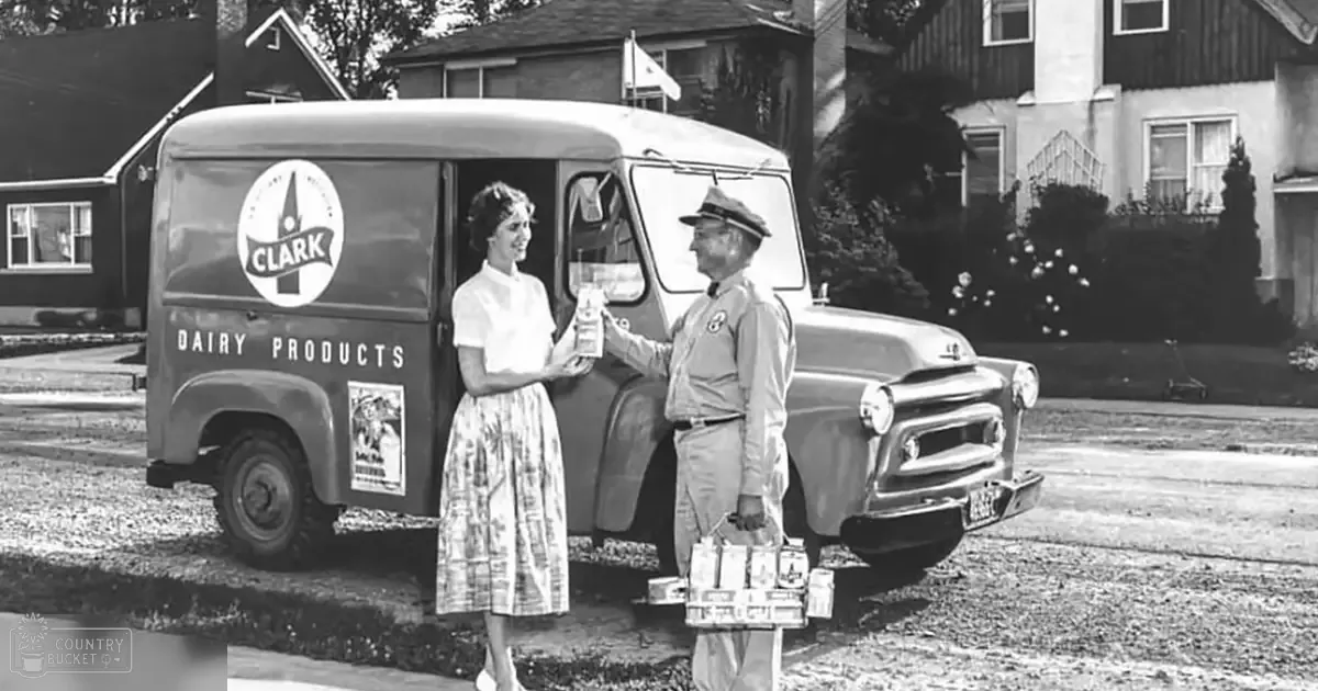 A milk delivery scene in an urban residential area with a vintage truck labeled 'Clark Dairy Products' parked on a street, surrounded by houses and trees under bright daylight.