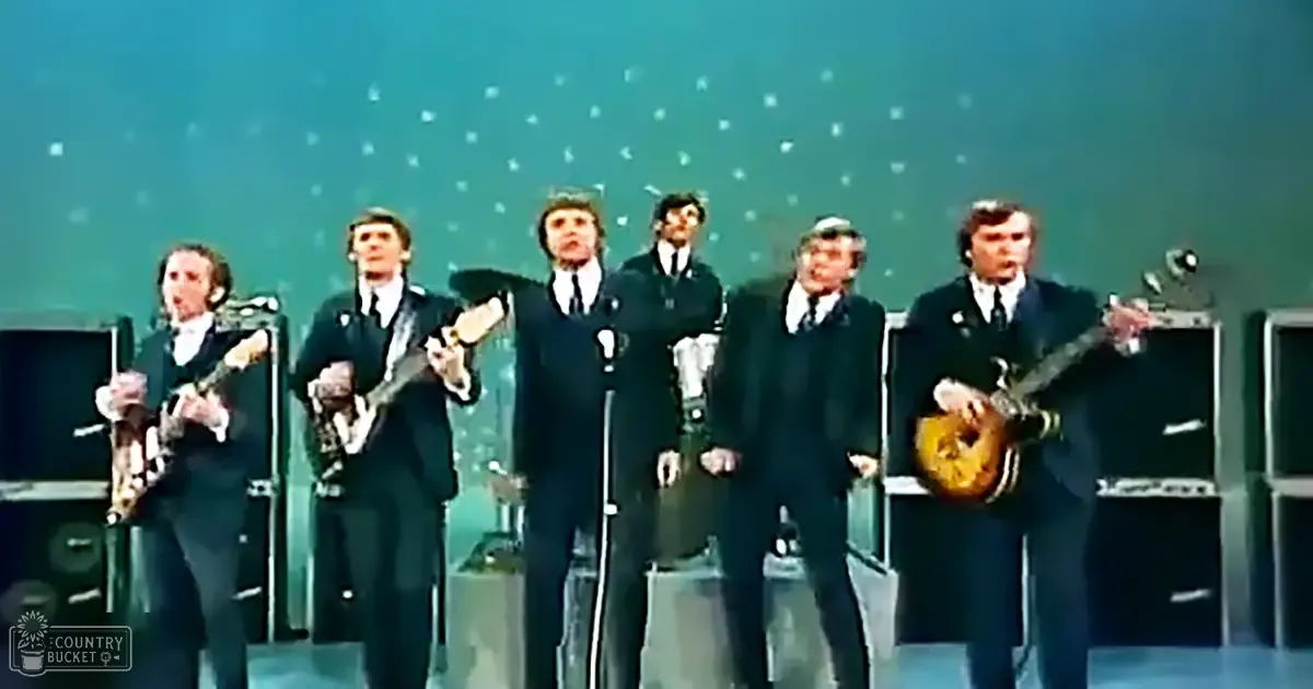 A musical performance group from the 1960s or 1970s in a studio setting with teal to green gradient backdrop, artificial stage lighting.