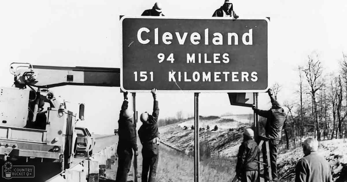 Workers installing a road sign near Cleveland in late fall or early spring with bare trees and daytime lighting.