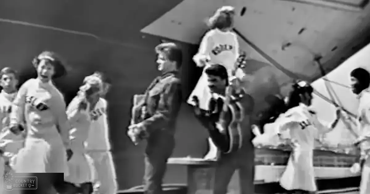 A group of individuals in front of an aircraft at what appears to be an airport or airfield setting; a child wearing a white dress with ruffles and a dark belt, an adult female holding something in her hands, a young adult male in military-style uniform with epaulets, another person wearing a shirt with "JET" printed on it, and a woman dressed in light-colored outfit with headpiece standing outdoors.