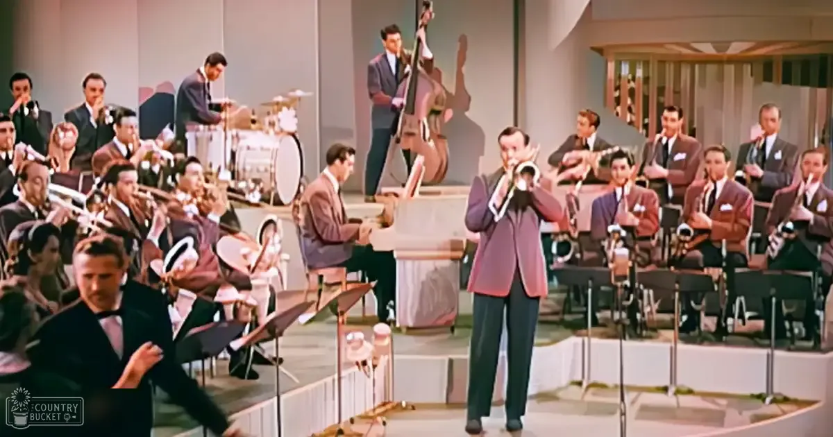 A jazz musician playing trumpet in front of an orchestra at a concert hall with bright stage lighting and formal attire typical of mid-20th-century musicians.