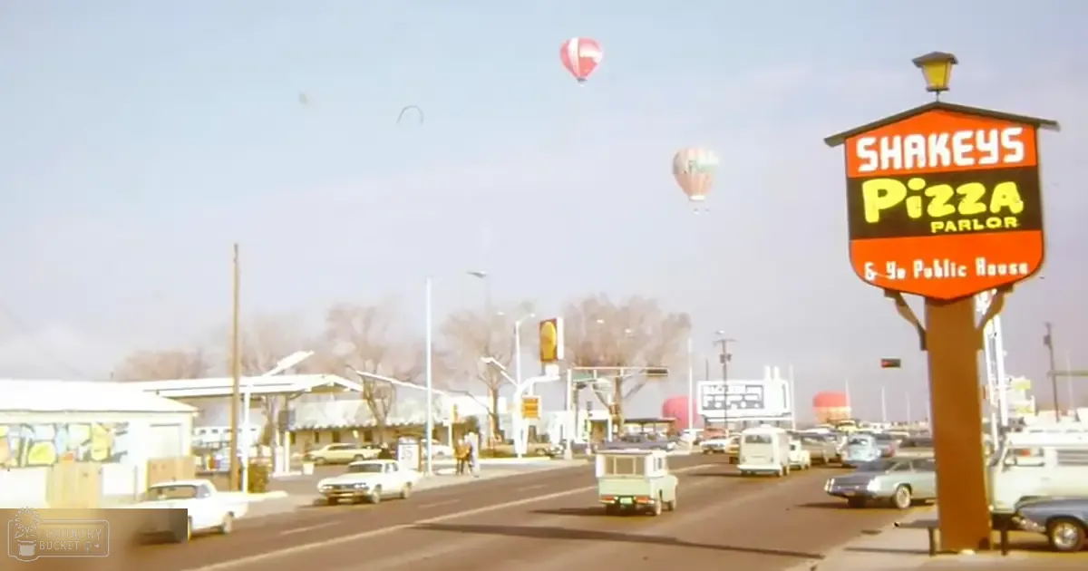 Urban scene with Shakey's Pizza Parlor sign, vintage cars, hot air balloons in late fall or early spring day