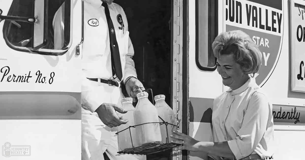 Sun Valley milk delivery scene with an adult male in white shirt and tie, holding a tray of glass milk bottles with a middle-aged woman in light-colored blouse or dress. The setting is outdoors on a sunny day.