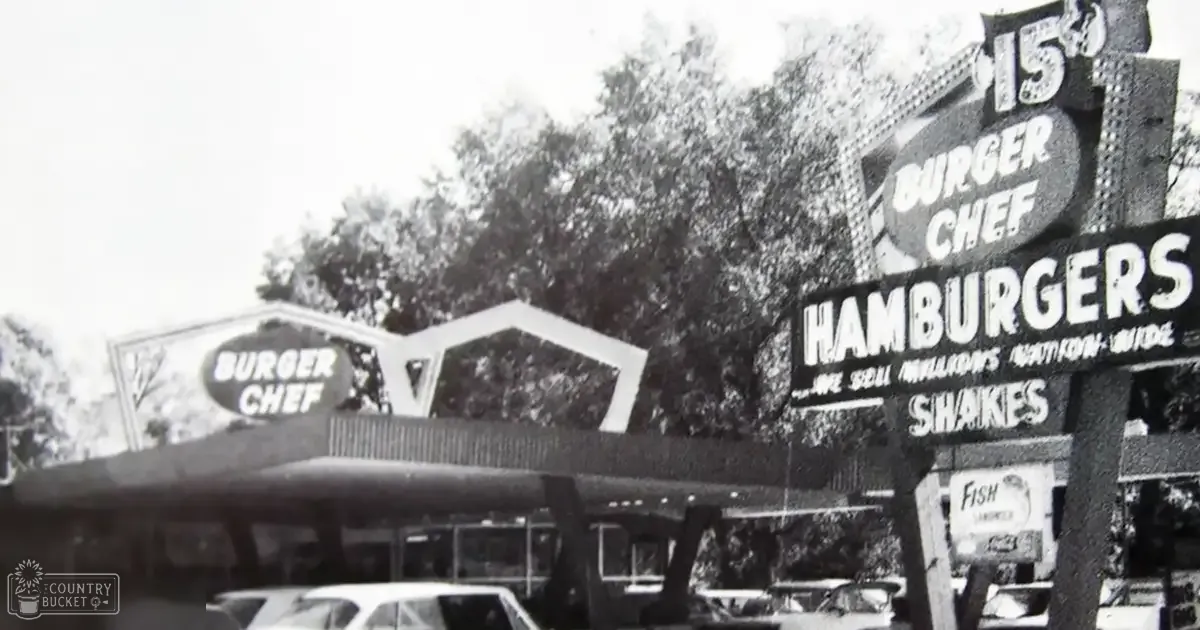 Burger Chef sign with prices in an outdoor setting with trees and parked cars.