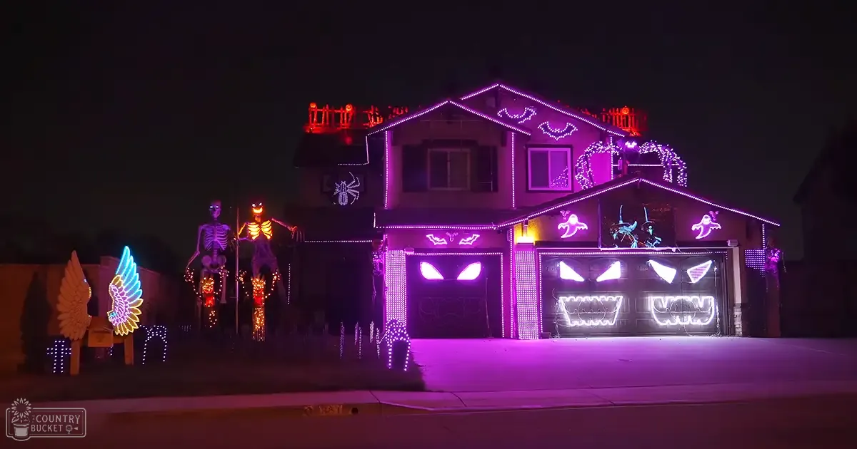 A Halloween-themed house adorned with spooky decorations, glowing lights, and illuminated figures in an urban residential neighborhood at night.