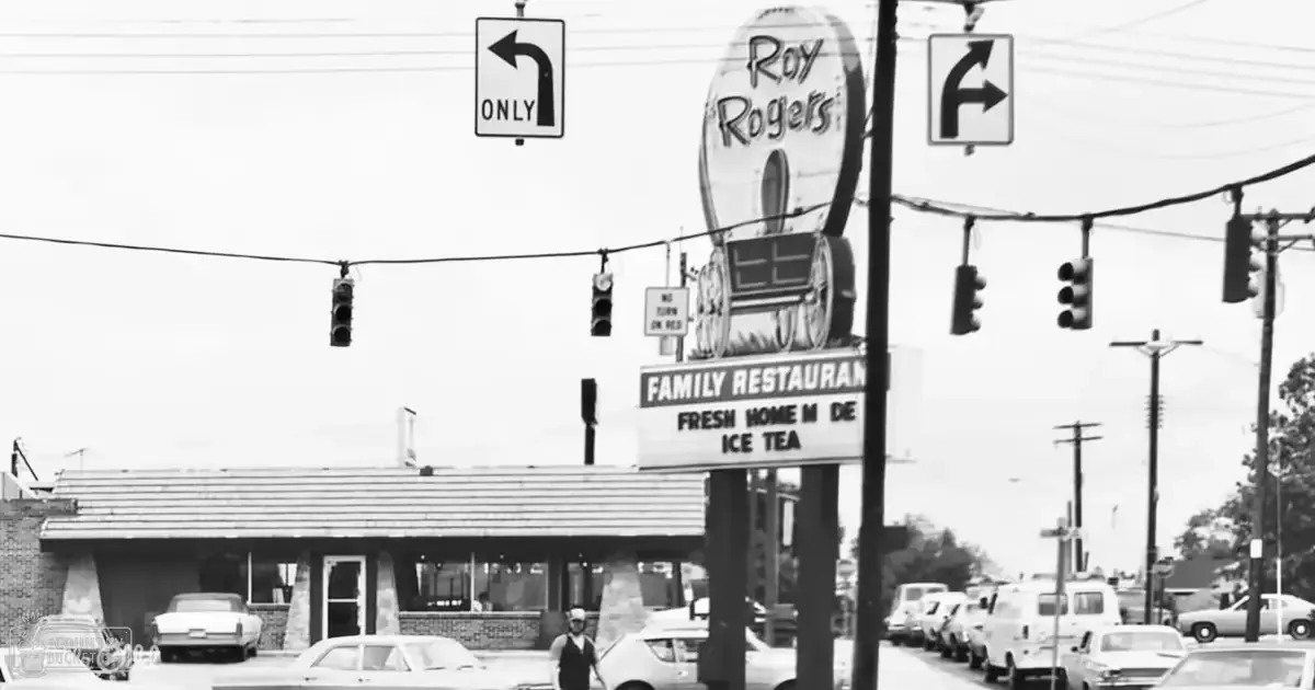 Roy Rogers Family Restaurant sign with wagon logo in an urban street scene during spring or summer day; vintage cars parked outside
