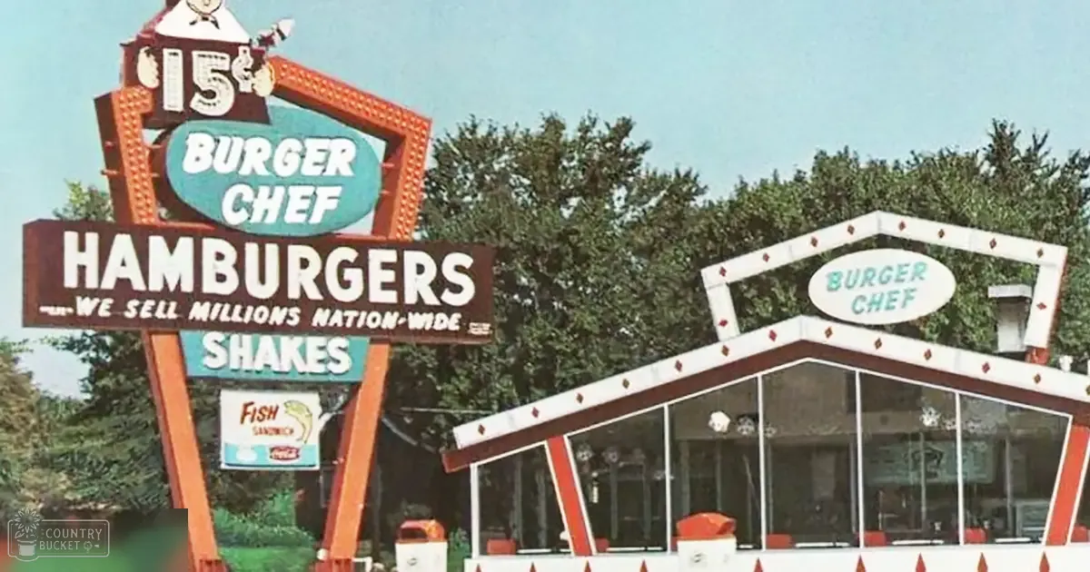 An outdoor Burger Chef restaurant sign with retro design and text advertising hamburgers, shakes, and fish sandwiches; trees and clear sky in background indicate daytime spring or summer setting