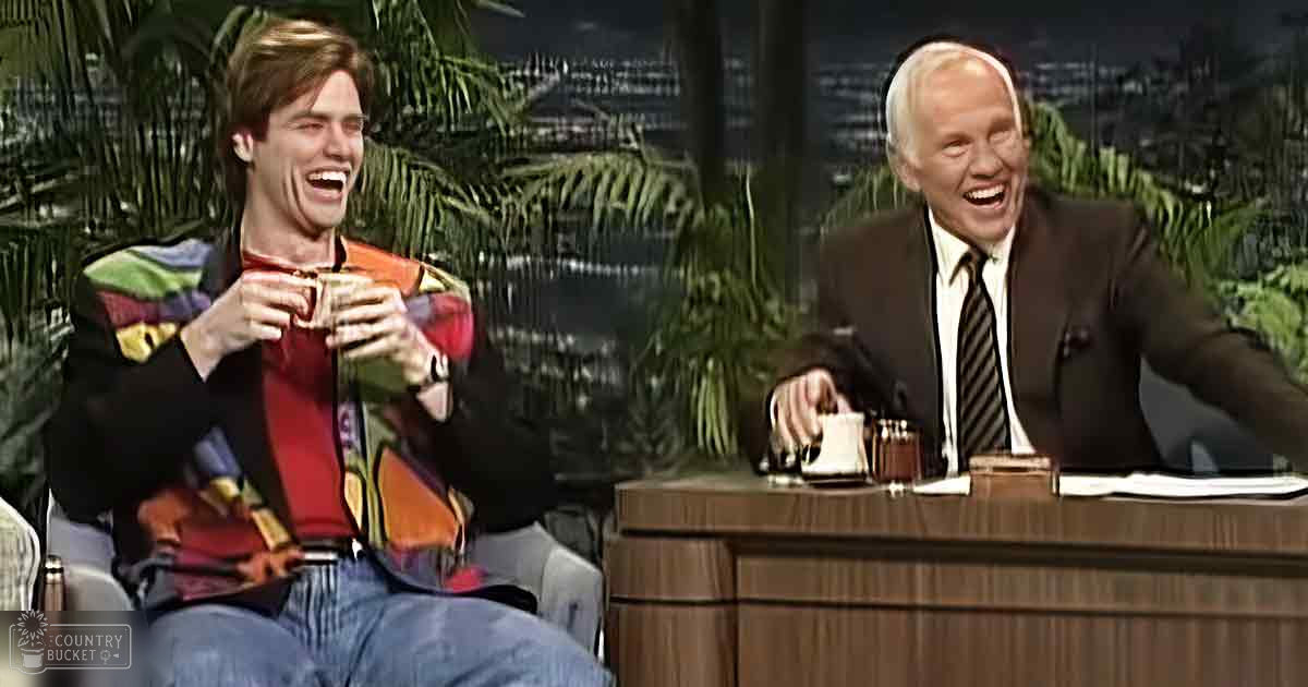 Young adult male in colorful, patterned jacket over red shirt with collar and blue jeans, middle-aged or older man wearing dark suit with white dress shirt and striped tie. Indoor studio setting with palm trees and cityscape backdrop at night.