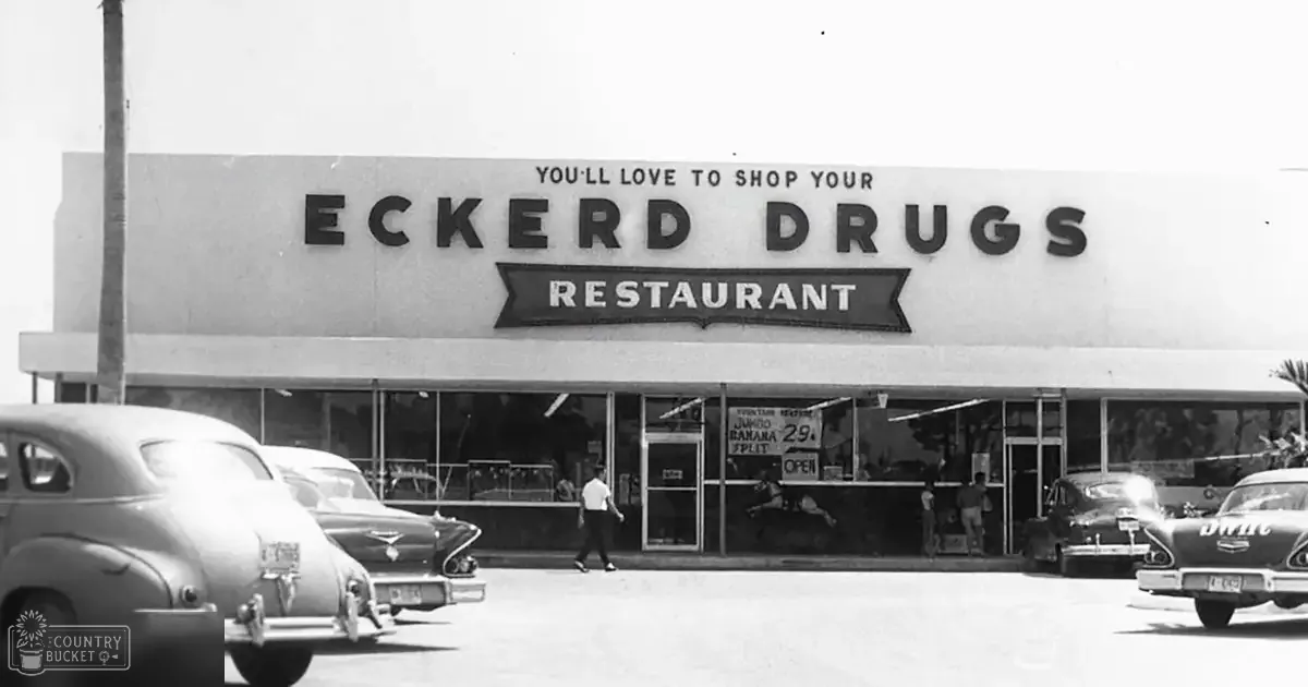 Urban setting with vintage Eckerd Drugs store and mid-20th century cars parked on the street; palm trees suggest warm climate, clear sky indicates daytime.
