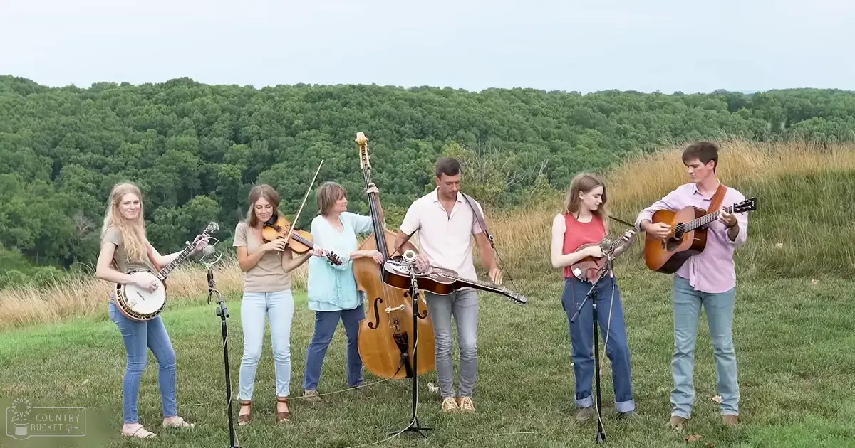 A group of young adult musicians performing outdoors in a grassy field with trees in the background during spring or summer.