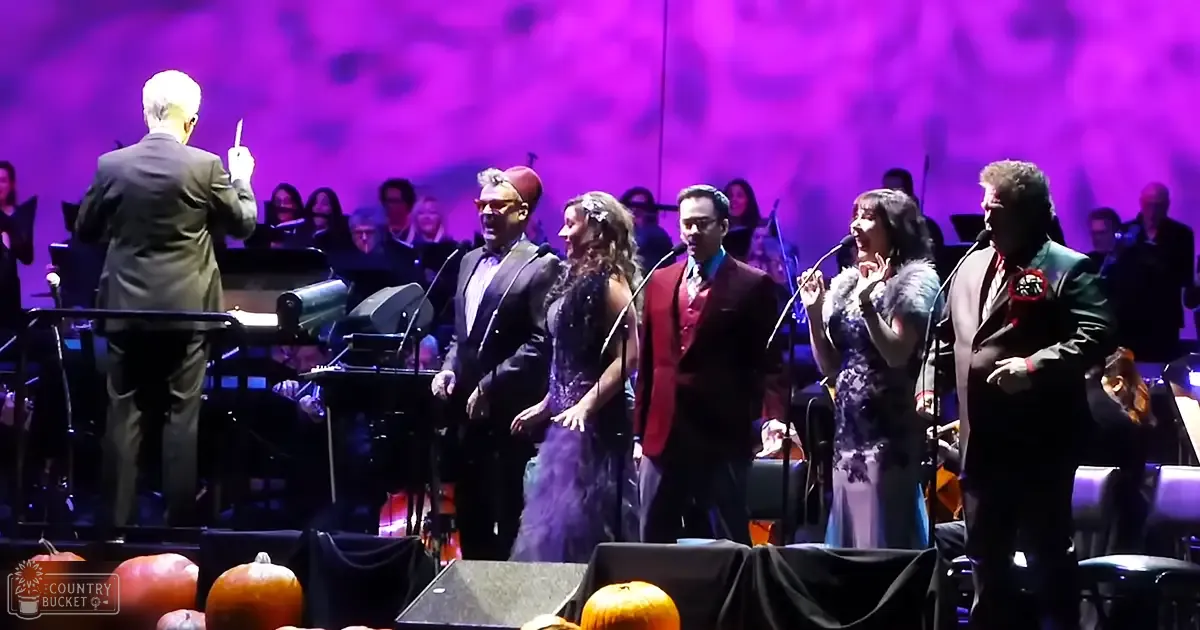 A musical performance at a concert hall with singers and an orchestra with pumpkins on stage.
