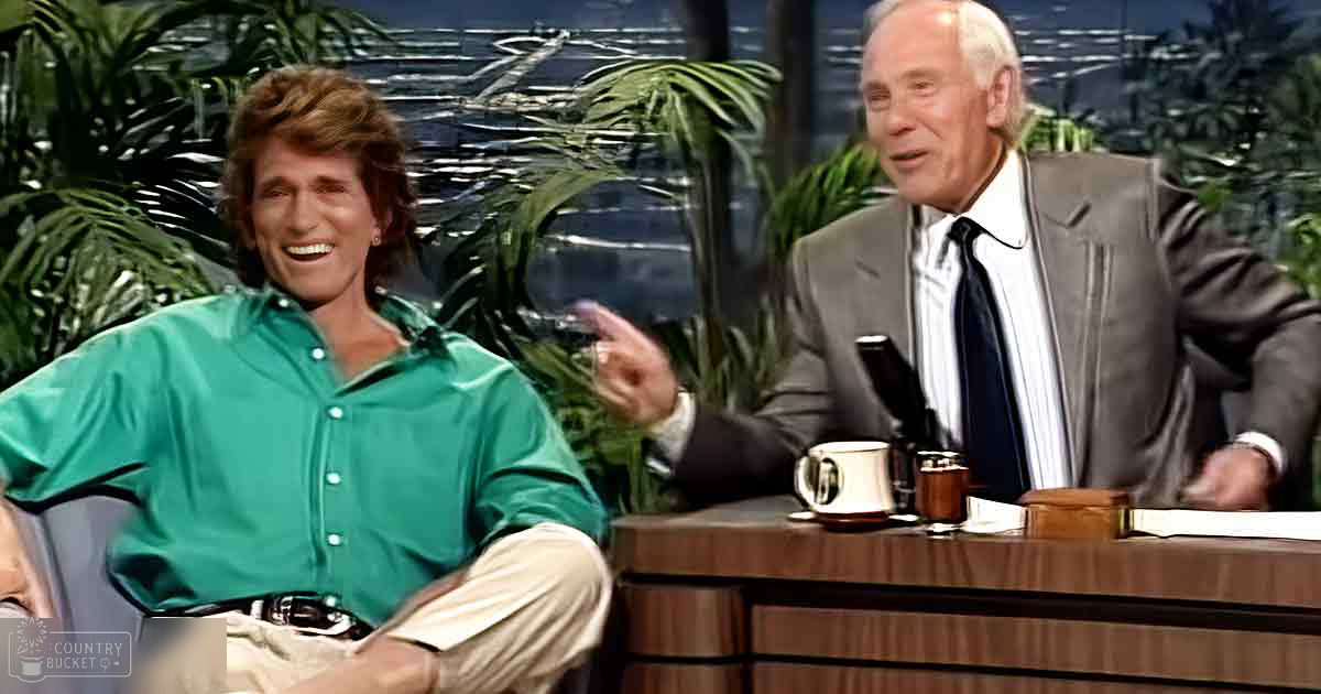 Adult male interview guest wearing a green button-up shirt, beige pants, and black belt; older adult male in a dark suit jacket over a white collared shirt and tie, in an indoor studio setting with decorative plants.