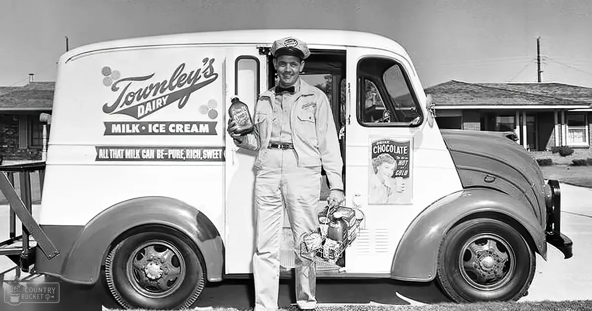 A young adult male milkman in white overalls delivers milk using a vintage Townley's Dairy panel van with 'Milk • Ice Cream' text, set against a residential neighborhood backdrop under bright daylight.
