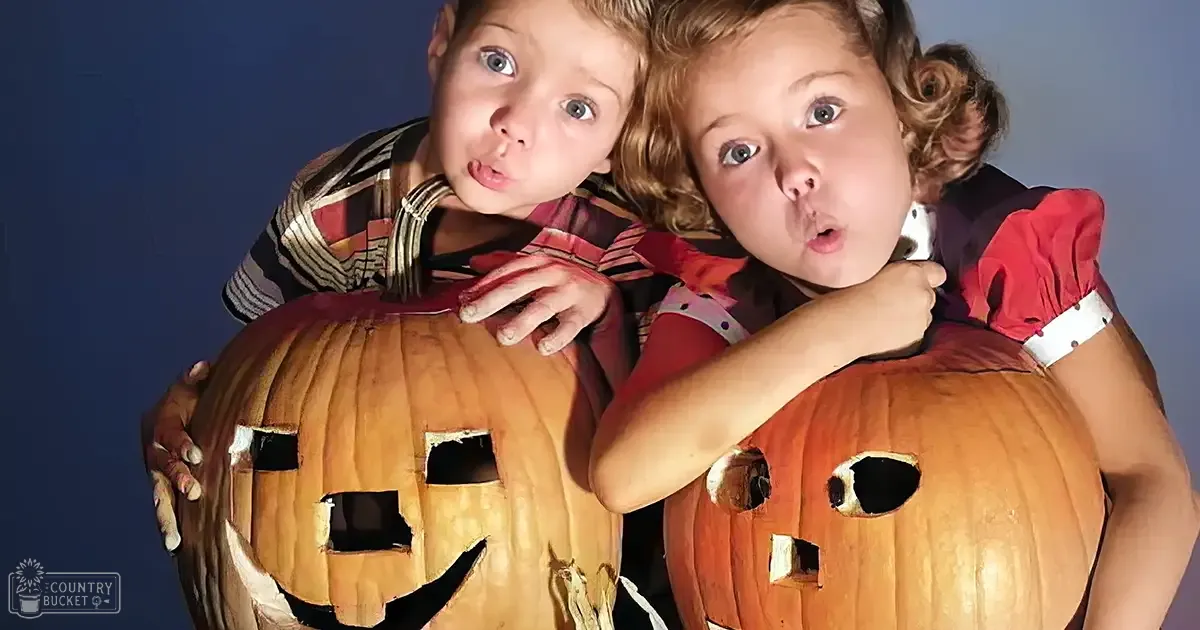 Two toddlers in a Halloween-themed setting, wearing striped shirts and red dresses against a plain blue backdrop.