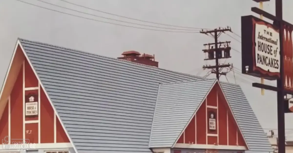 A view of an urban area with a distinctive triangular-roofed building, sign for 'The International House of Pancakes', utility pole, cloudy sky.
