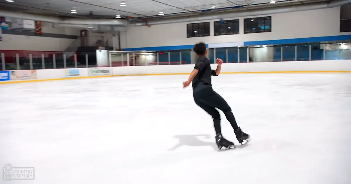 A young adult male skating in an indoor ice rink with smooth white flooring, artificial lighting, and advertisements on the walls.