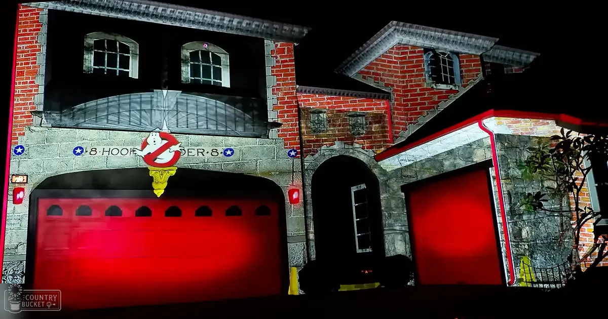 A ghostly, eerie glow illuminates a themed firehouse with red garage doors at night, part of a Halloween display or attraction.