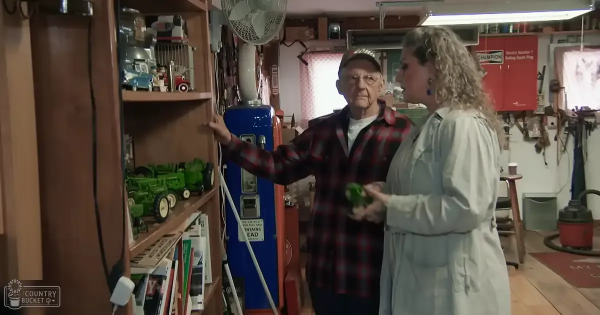 An older adult male in a workshop or garage setting with tools and collectibles around him.