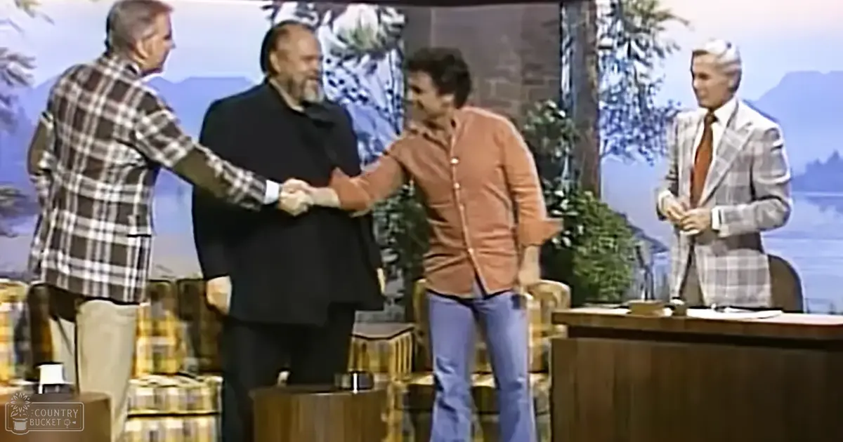 Four individuals interacting in a studio setting with a scenic outdoor backdrop, suggesting a daytime talk show broadcast.