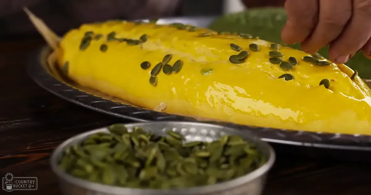 A freshly cooked yellow omelette garnished with pumpkin seeds, placed on a black plate next to a bowl of additional pumpkin seeds in a kitchen or dining area setting.