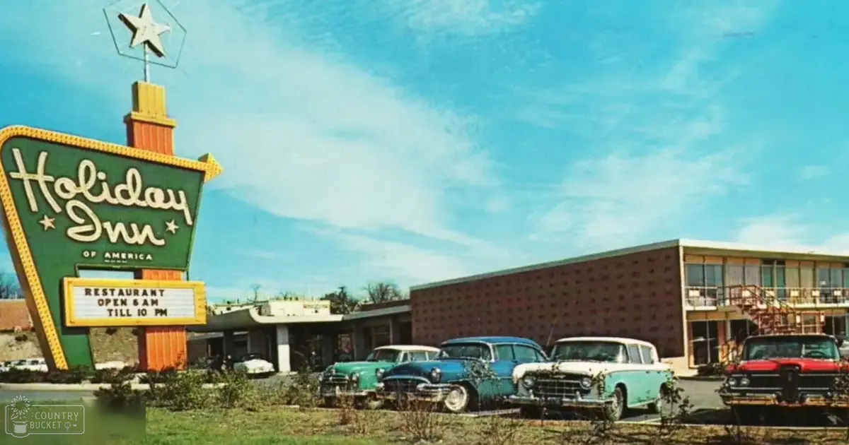 Holiday Inn sign in front of an American hotel with mid-20th century vintage cars parked outside on a clear day during spring or summer.