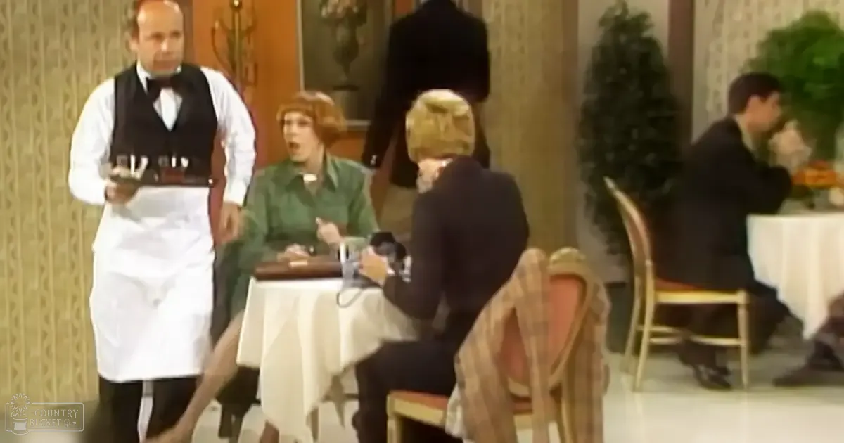An adult male waiter in a white shirt, black vest, bow tie, and apron stands at a table with an older seated woman wearing a green dress and dark skirt in the foreground. A Christmas tree is visible in the background, suggesting winter season.