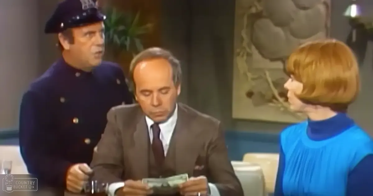 A mid-20th-century indoor scene with a man in a dark brown suit seated at a table, flanked by two other individuals, including one in a blue uniform and another in a sleeveless blue top. The setting includes simple furniture and artwork, suggesting an older establishment.