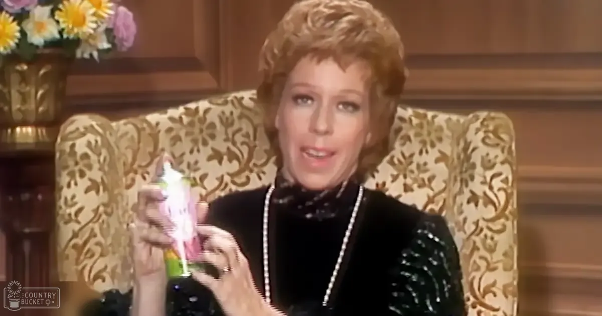 An older adult woman wearing a black velvet top with sequins and beads, pearl necklace, bracelet, seated on a patterned armchair with floral design and gold accents in an indoor studio setting.