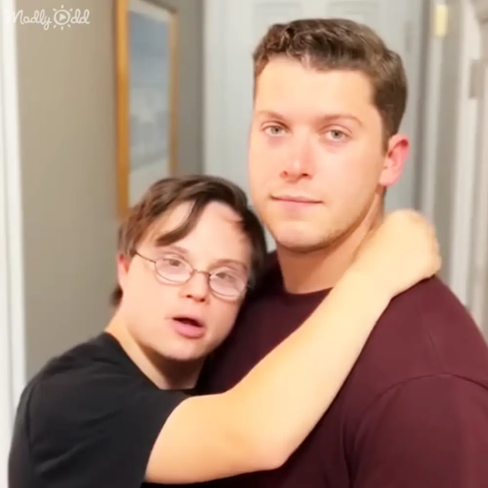 A young adult male and a teenager wearing casual t-shirts indoors, likely in a home setting with natural daylight.