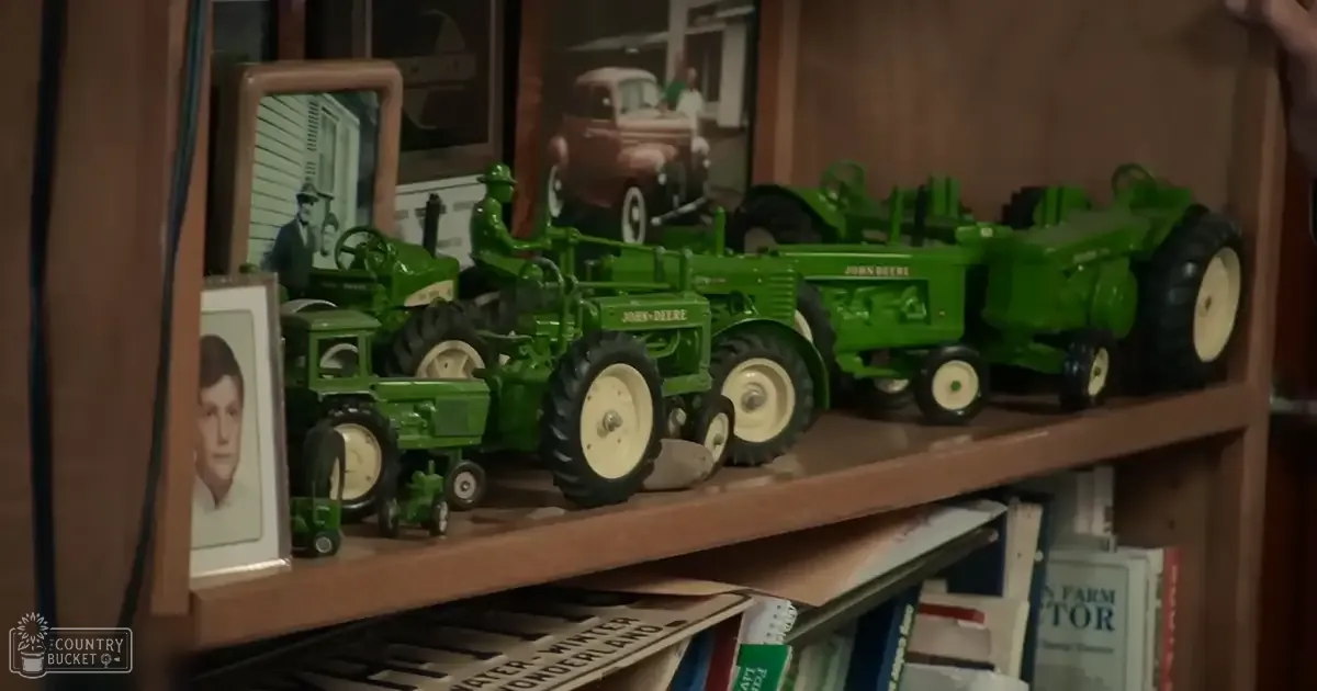 Indoor scene with model tractors, framed photographs, and books in a hobby space or living area during daytime.
