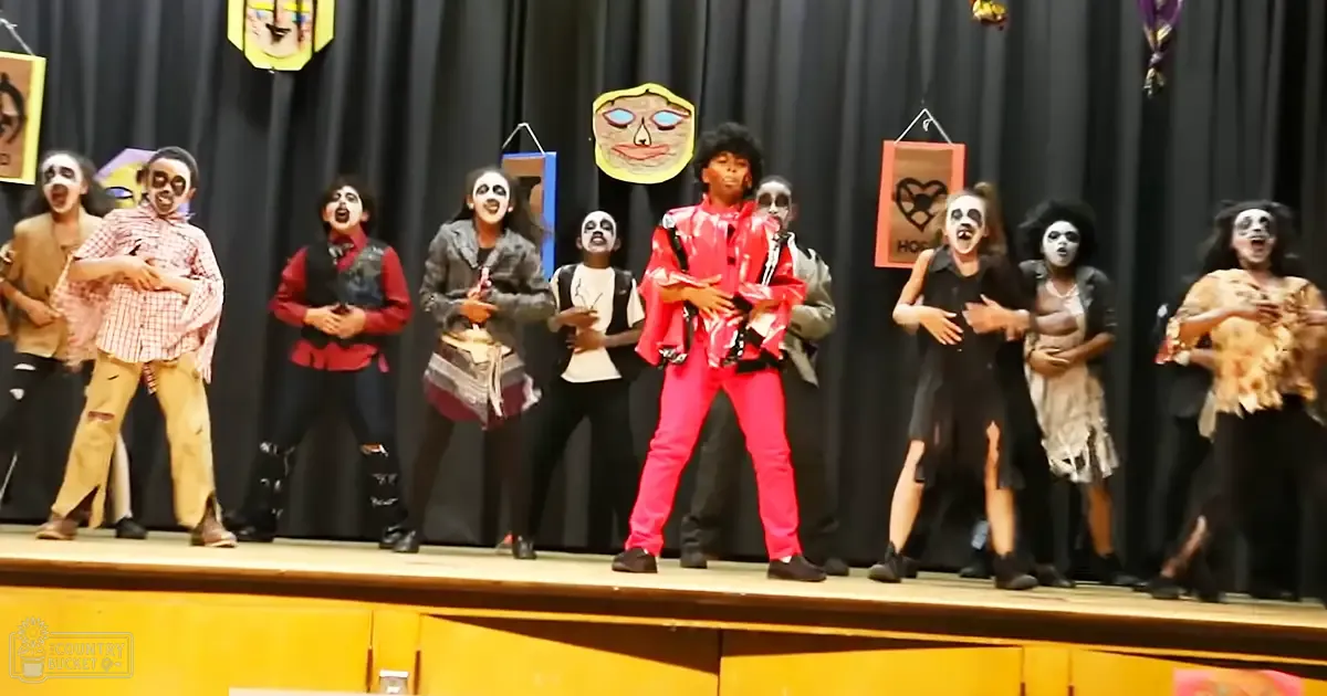 Group of children performing in a school or community event at an indoor stage with dark curtain backdrop.