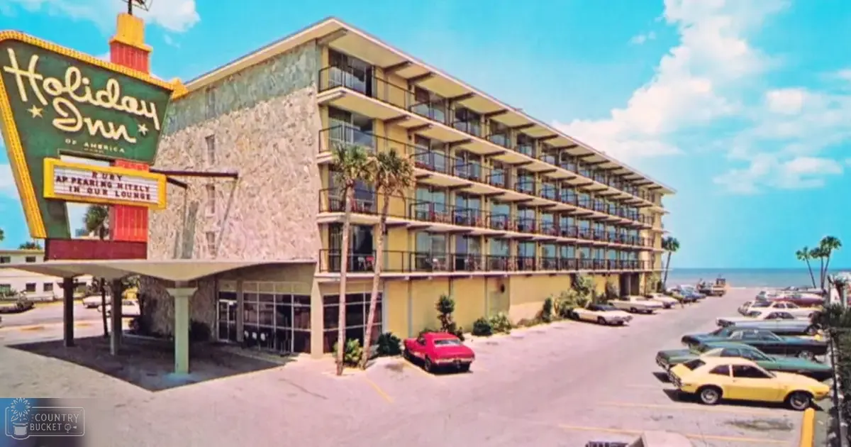 Holiday Inn hotel sign at a beachside location with clear skies and multiple parked vehicles, daytime setting.