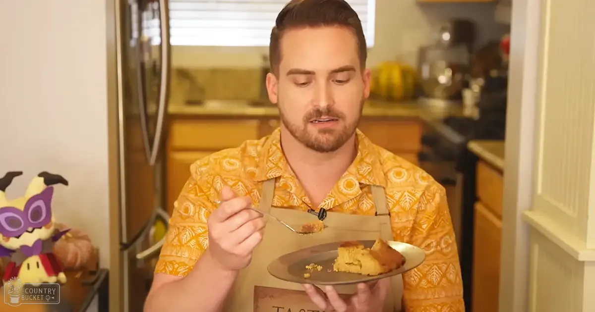 A young adult male wearing a yellow Hawaiian shirt with leafy patterns in an indoor kitchen setting, holding a slice of cake or pie.